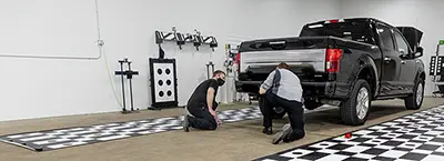 Technicians performing a rear camera ADAS calibration on a truck to ensure systems function properly after collision repair at a body shop