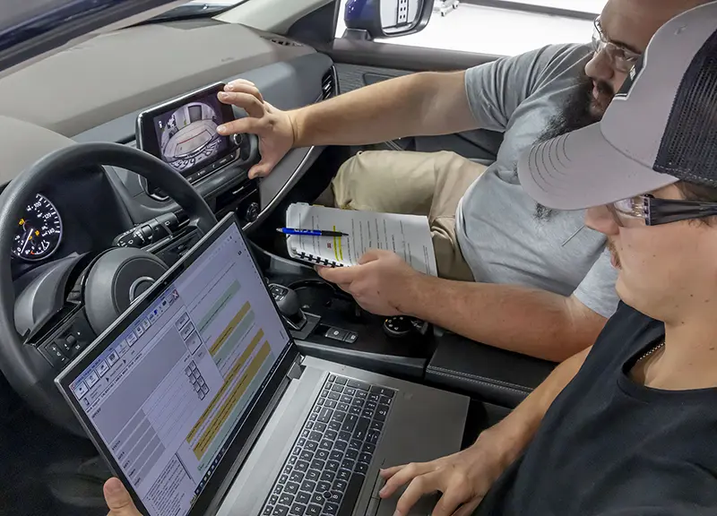 Technicians in a car testing a camera for proper ADAS calibration to ensure systems function properly after collision or accident repair